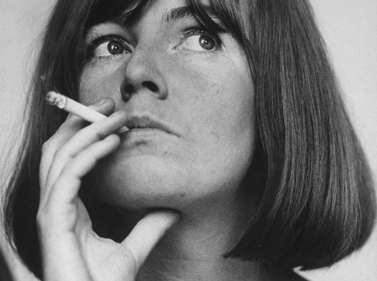 A black-and-white portrait of a woman with a bob, holding a lit cigarette and looking up thoughtfully.