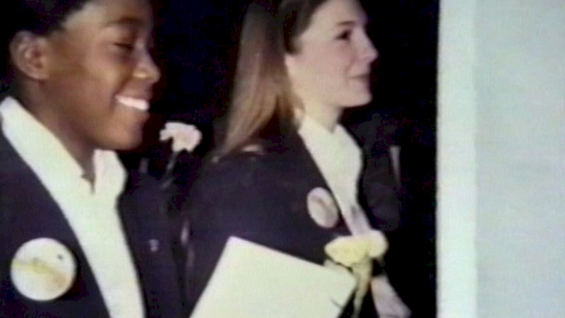 Two young people in blazers and white shirts walking side by side, smiling.